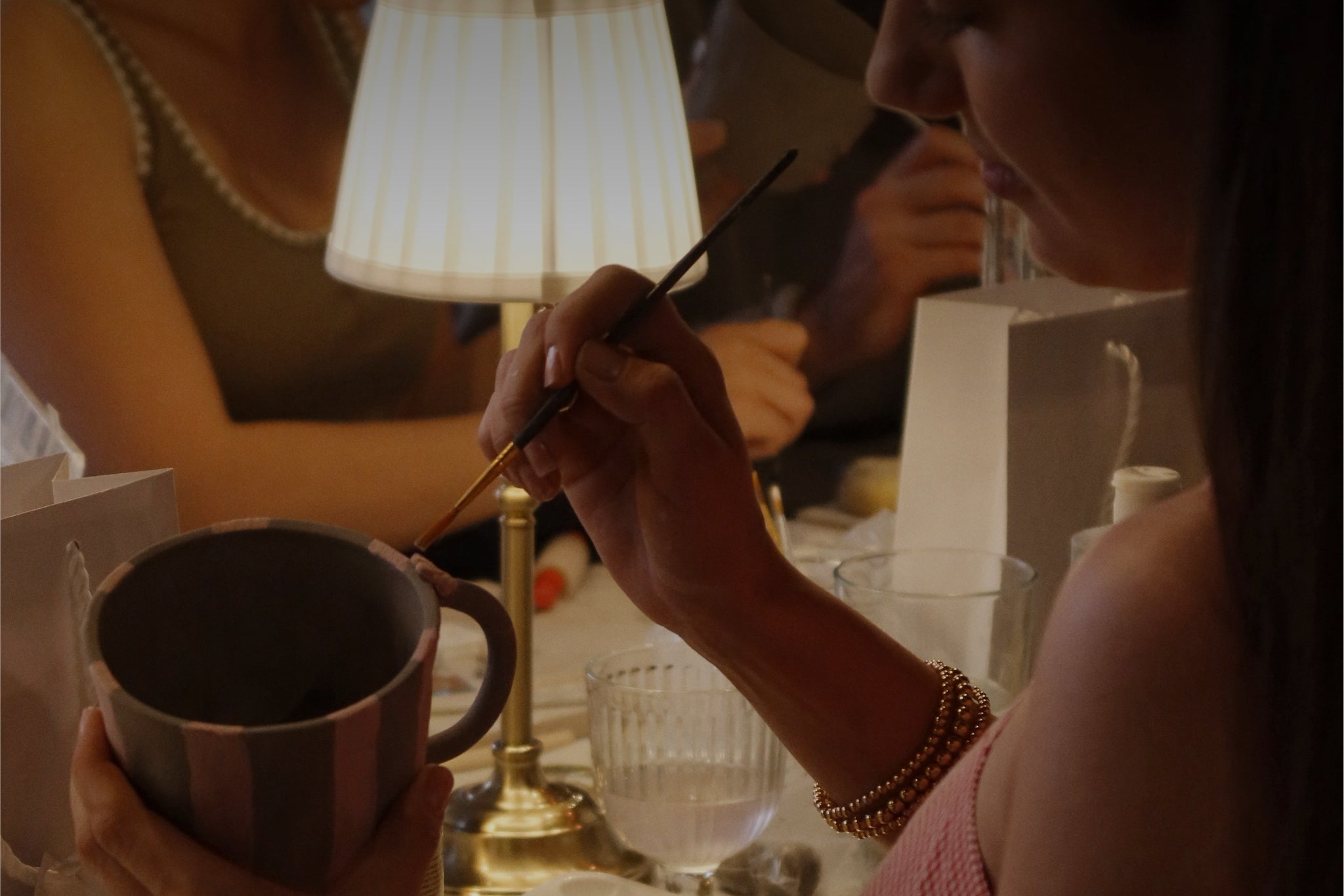 Person painting a ceramic mug whilst at an aesthetic romantic candle lit table.